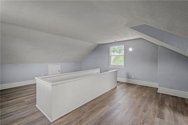 additional living space with a textured ceiling, lofted ceiling, baseboards, and wood finished floors