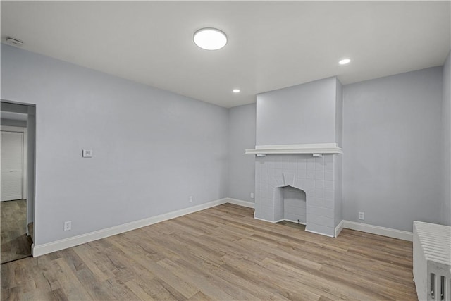 unfurnished living room featuring a tiled fireplace, recessed lighting, baseboards, and wood finished floors