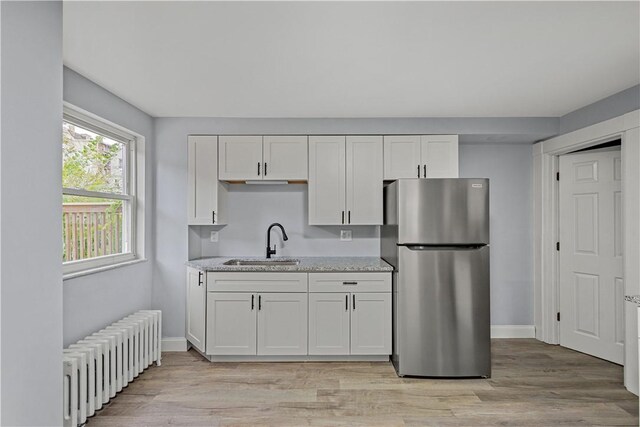 kitchen featuring radiator, freestanding refrigerator, a sink, white cabinets, and light wood-style floors