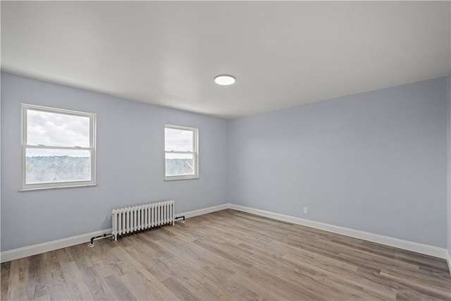 unfurnished room featuring radiator heating unit, wood finished floors, and baseboards