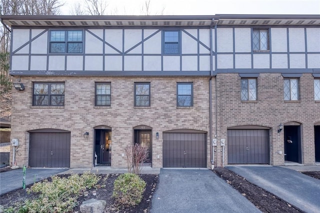 view of property with aphalt driveway, stucco siding, an attached garage, and brick siding