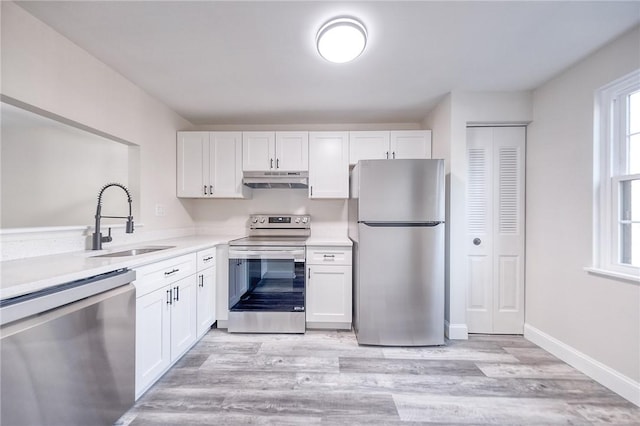 kitchen with under cabinet range hood, light countertops, appliances with stainless steel finishes, white cabinetry, and a sink