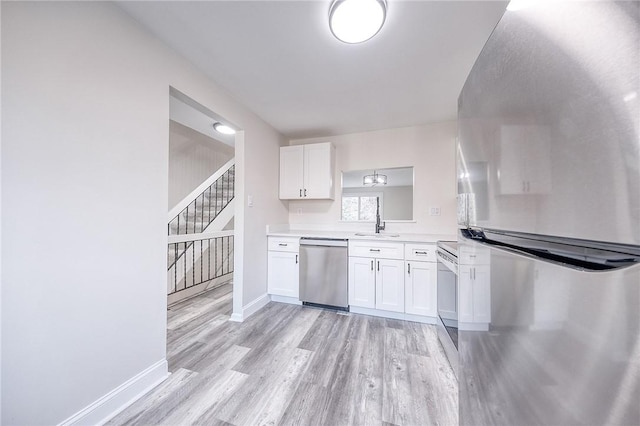 kitchen with a sink, light wood-style floors, appliances with stainless steel finishes, white cabinets, and light countertops