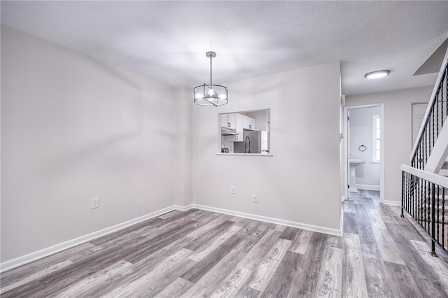 unfurnished dining area featuring stairs, wood finished floors, baseboards, and a chandelier