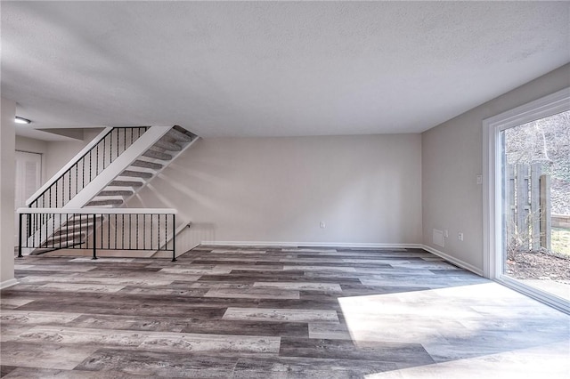 unfurnished living room with stairs, wood finished floors, baseboards, and a textured ceiling