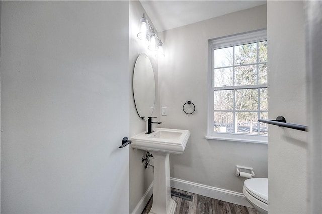 half bathroom with visible vents, plenty of natural light, toilet, and baseboards