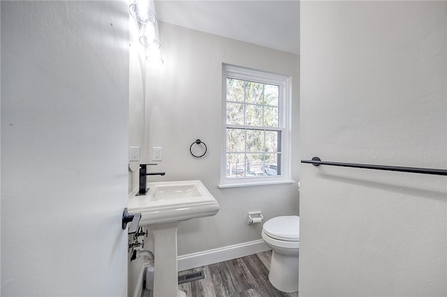 half bath with toilet, wood finished floors, and baseboards