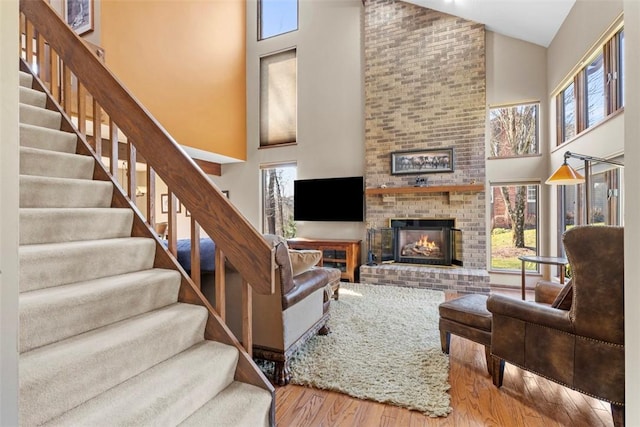 living area featuring a fireplace, stairway, wood finished floors, and high vaulted ceiling