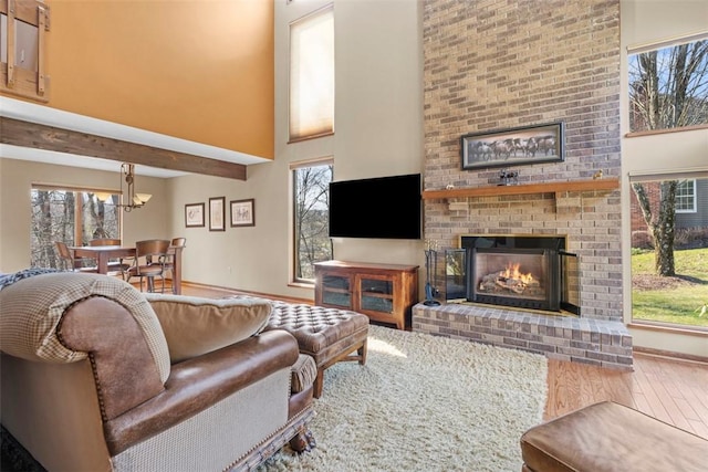 living room featuring baseboards, beamed ceiling, a fireplace, a towering ceiling, and wood finished floors