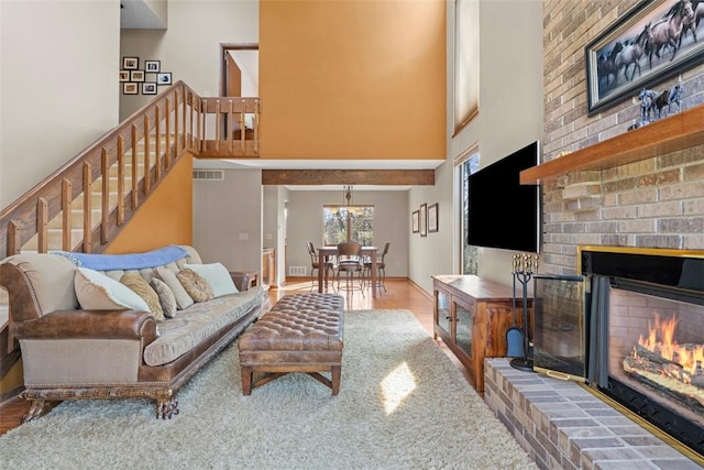 living room with visible vents, wood finished floors, a brick fireplace, a towering ceiling, and stairs