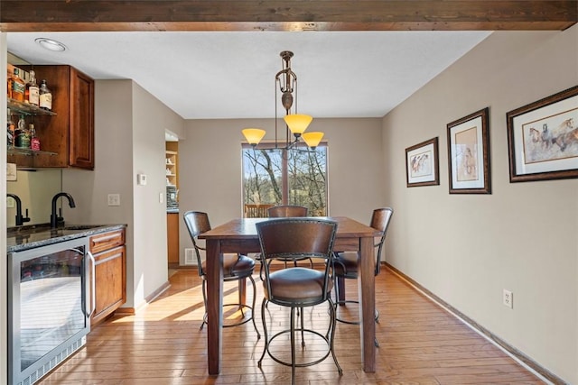 dining space with beverage cooler, light wood-style flooring, indoor wet bar, and baseboards