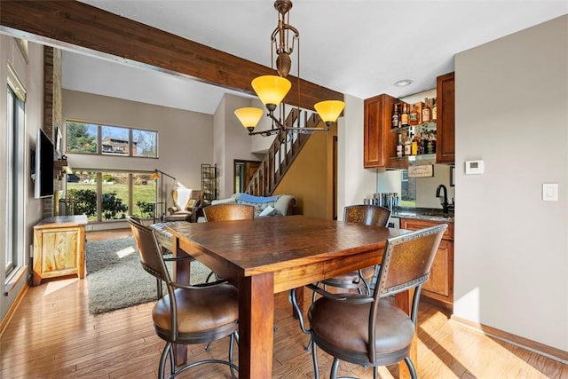 dining space featuring beam ceiling, stairway, wet bar, and light wood-type flooring