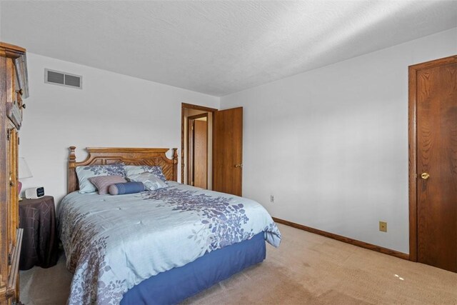 bedroom featuring a textured ceiling, light colored carpet, visible vents, and baseboards