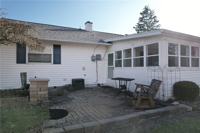 back of house featuring roof with shingles, a chimney, and a patio area