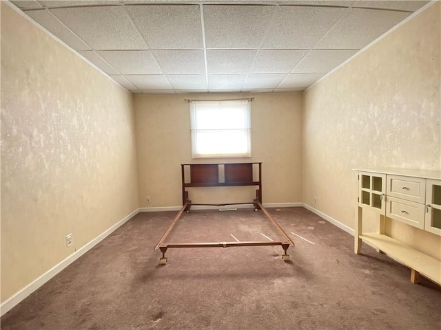 unfurnished bedroom featuring a textured wall, baseboards, a drop ceiling, and carpet floors