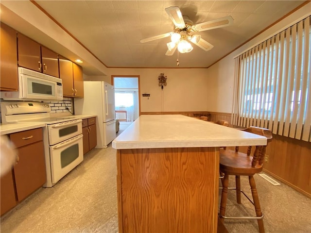 kitchen featuring white appliances, wooden walls, a kitchen island, ornamental molding, and wainscoting