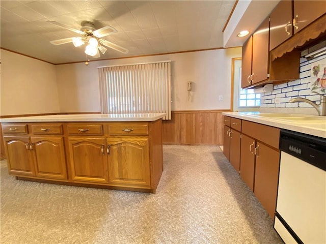 kitchen with a wainscoted wall, a sink, wooden walls, light countertops, and dishwasher