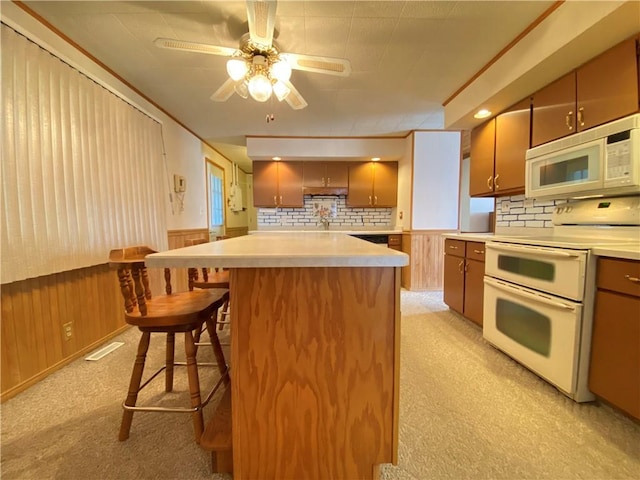 kitchen with white appliances, a wainscoted wall, wood walls, light carpet, and a kitchen breakfast bar