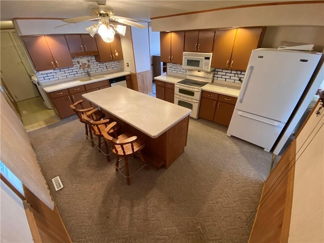 kitchen with tasteful backsplash, a center island, ceiling fan, light countertops, and white appliances