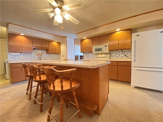 kitchen with tasteful backsplash, white appliances, a breakfast bar area, light countertops, and ceiling fan