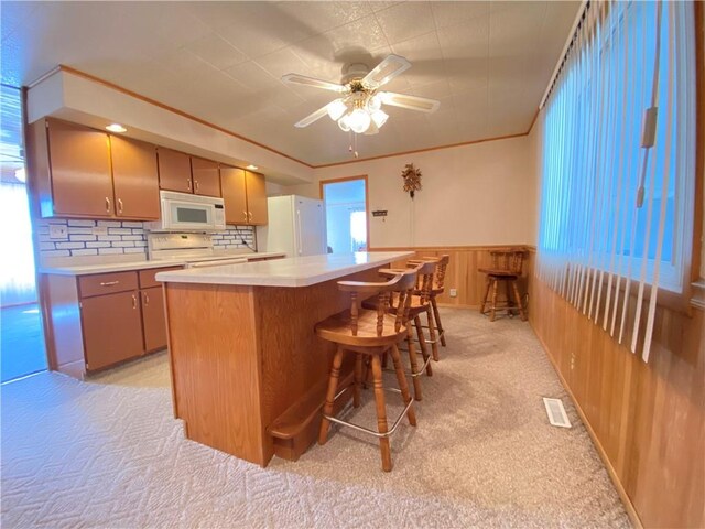 kitchen with white appliances, a kitchen island, light countertops, crown molding, and light colored carpet