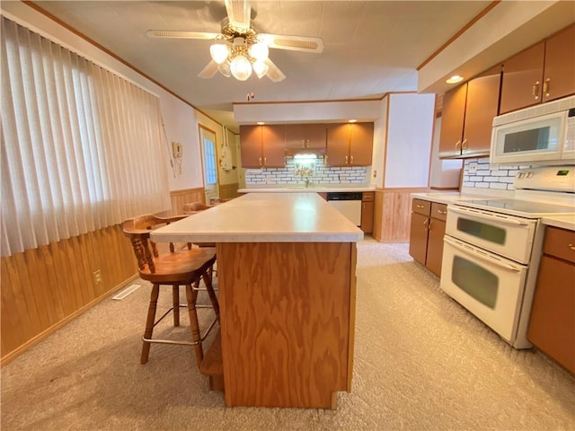 kitchen with white appliances, a wainscoted wall, a breakfast bar, light countertops, and wood walls