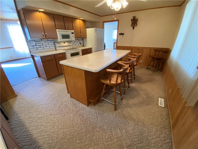 kitchen with white appliances, crown molding, a wainscoted wall, and light countertops