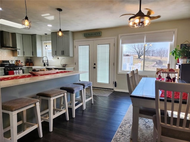 kitchen featuring dark wood-type flooring, gas stove, wall chimney exhaust hood, light countertops, and decorative backsplash