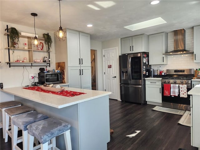 kitchen featuring a kitchen breakfast bar, stainless steel appliances, a peninsula, wall chimney exhaust hood, and dark wood-style flooring