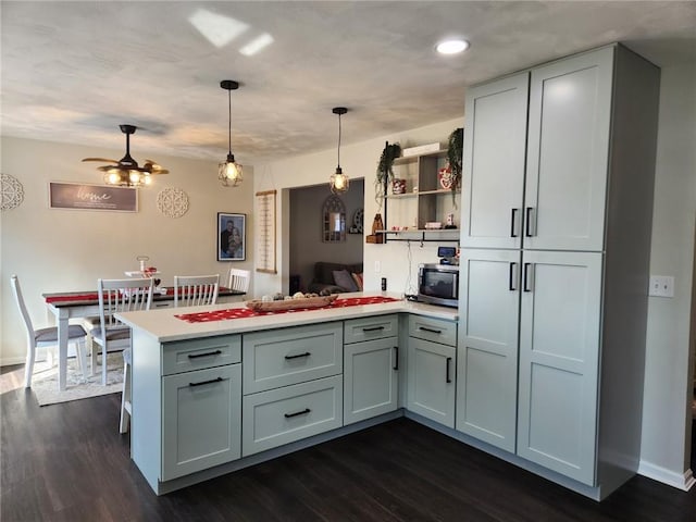 kitchen featuring open shelves, stainless steel microwave, dark wood finished floors, a peninsula, and light countertops