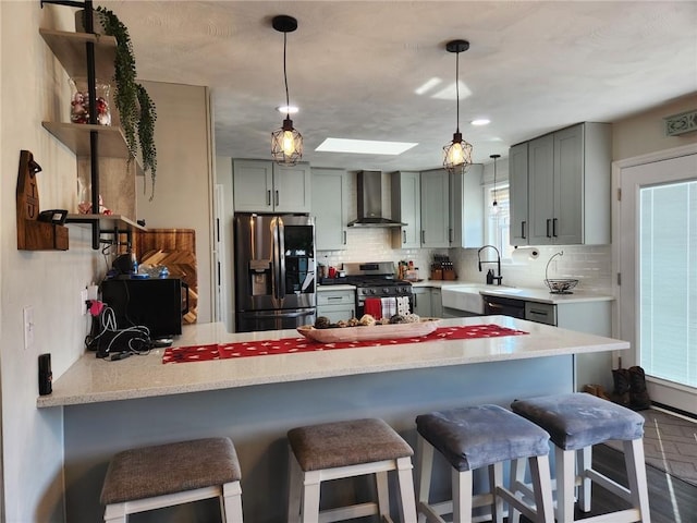 kitchen featuring a peninsula, a skylight, decorative backsplash, appliances with stainless steel finishes, and wall chimney exhaust hood