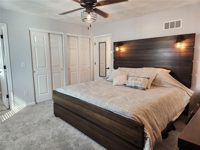 bedroom featuring a ceiling fan, baseboards, visible vents, multiple closets, and carpet flooring