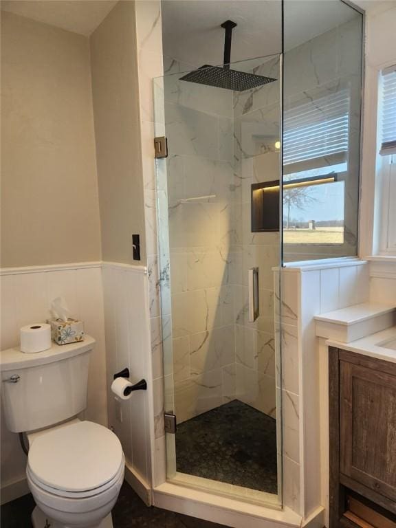 bathroom featuring a marble finish shower, a wainscoted wall, toilet, and vanity