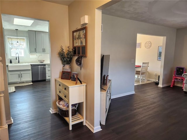 corridor featuring a skylight, dark wood-style floors, baseboards, and a sink