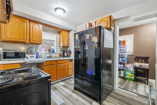 kitchen featuring brown cabinetry, a sink, black appliances, light countertops, and light wood-type flooring