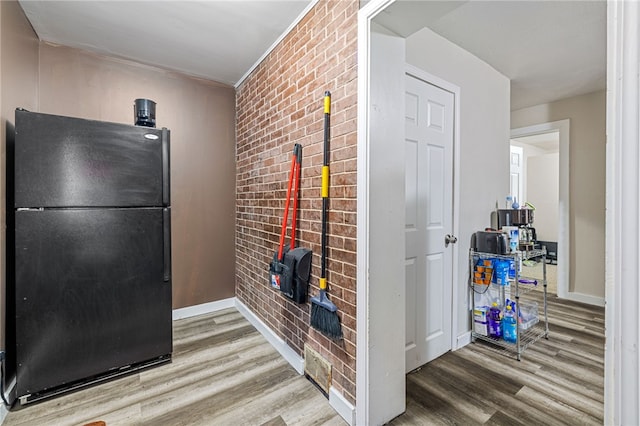 interior space with brick wall, freestanding refrigerator, baseboards, and wood finished floors