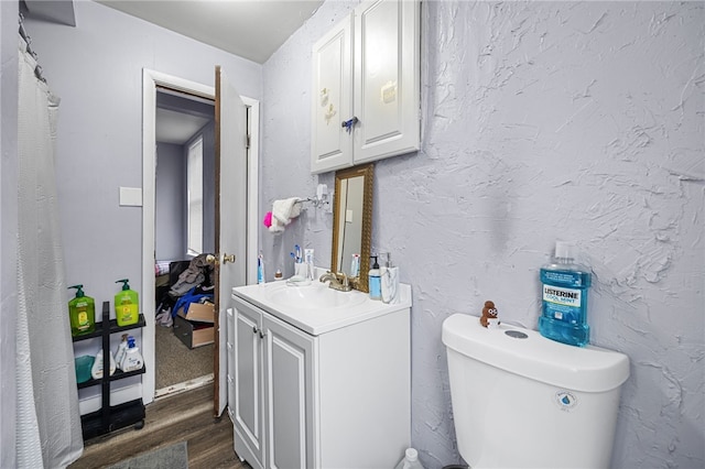 bathroom with wood finished floors, toilet, vanity, and a textured wall