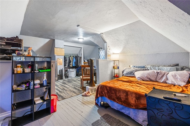 bedroom with vaulted ceiling, a textured wall, a closet, a textured ceiling, and wood-type flooring