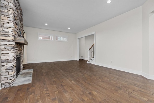 unfurnished living room with a stone fireplace, stairway, dark wood-type flooring, and baseboards