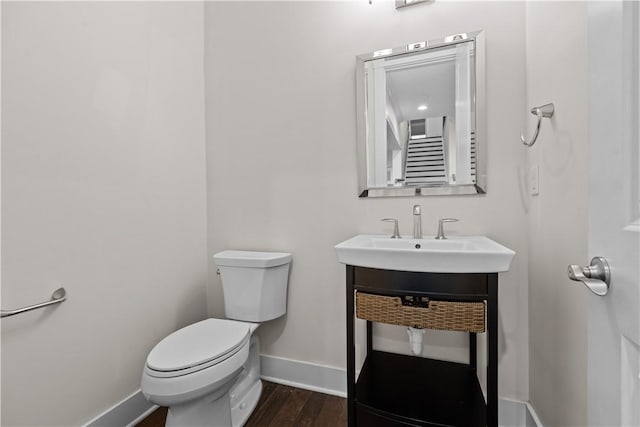 half bathroom with toilet, wood finished floors, baseboards, and a sink