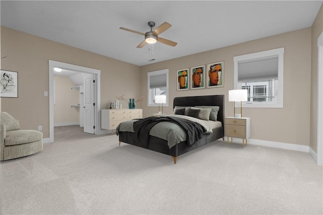 bedroom with light colored carpet, a ceiling fan, a walk in closet, and baseboards