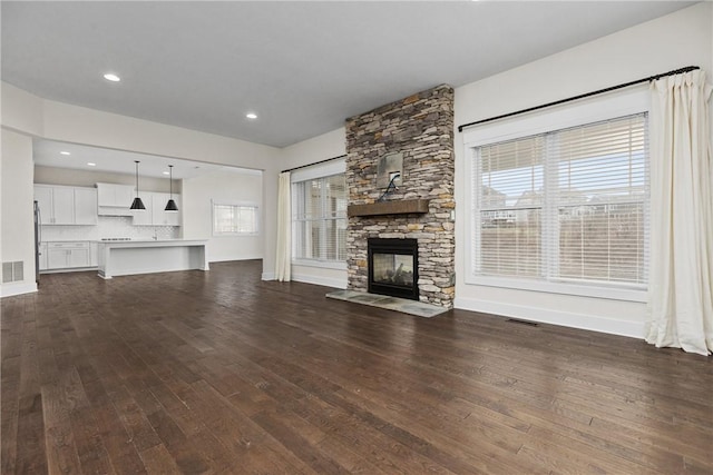 unfurnished living room featuring dark wood finished floors, visible vents, a fireplace, and baseboards