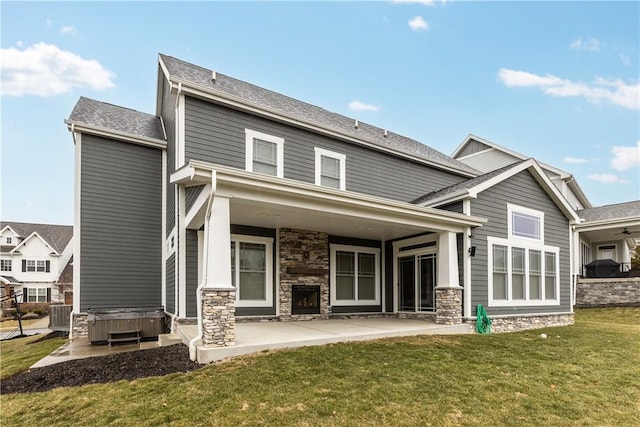 rear view of house with a hot tub, a lawn, cooling unit, stone siding, and a patio