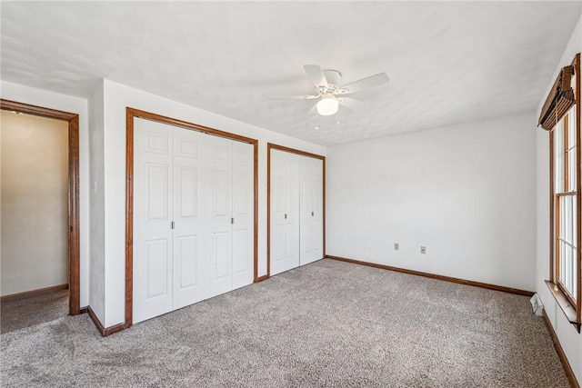 unfurnished bedroom featuring multiple windows, carpet, baseboards, and two closets