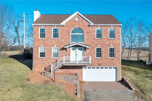 colonial house featuring brick siding, aphalt driveway, a front yard, a chimney, and a garage