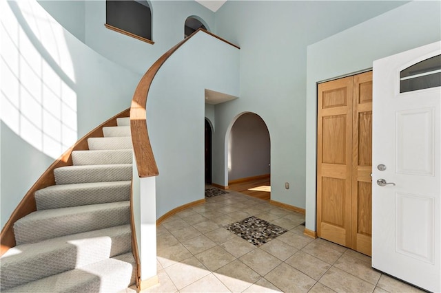 foyer featuring light tile patterned floors, baseboards, a high ceiling, arched walkways, and stairs