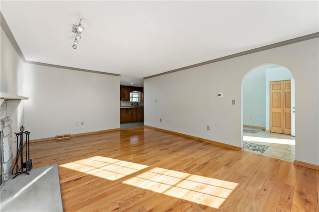 unfurnished living room featuring light wood finished floors, visible vents, a fireplace with raised hearth, baseboards, and arched walkways