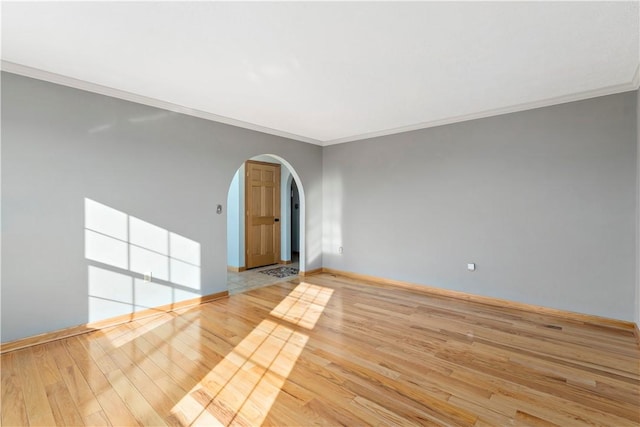 unfurnished room featuring arched walkways, crown molding, baseboards, and wood finished floors