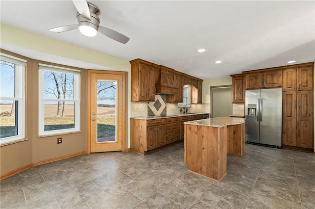 kitchen with light stone counters, a kitchen island, stainless steel fridge with ice dispenser, a sink, and tasteful backsplash