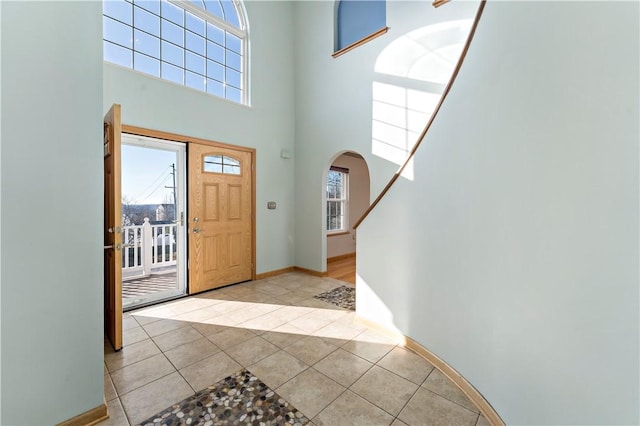 foyer entrance featuring light tile patterned flooring, baseboards, arched walkways, and a towering ceiling